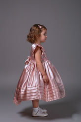 Young girl in a pink dress standing against a gray background