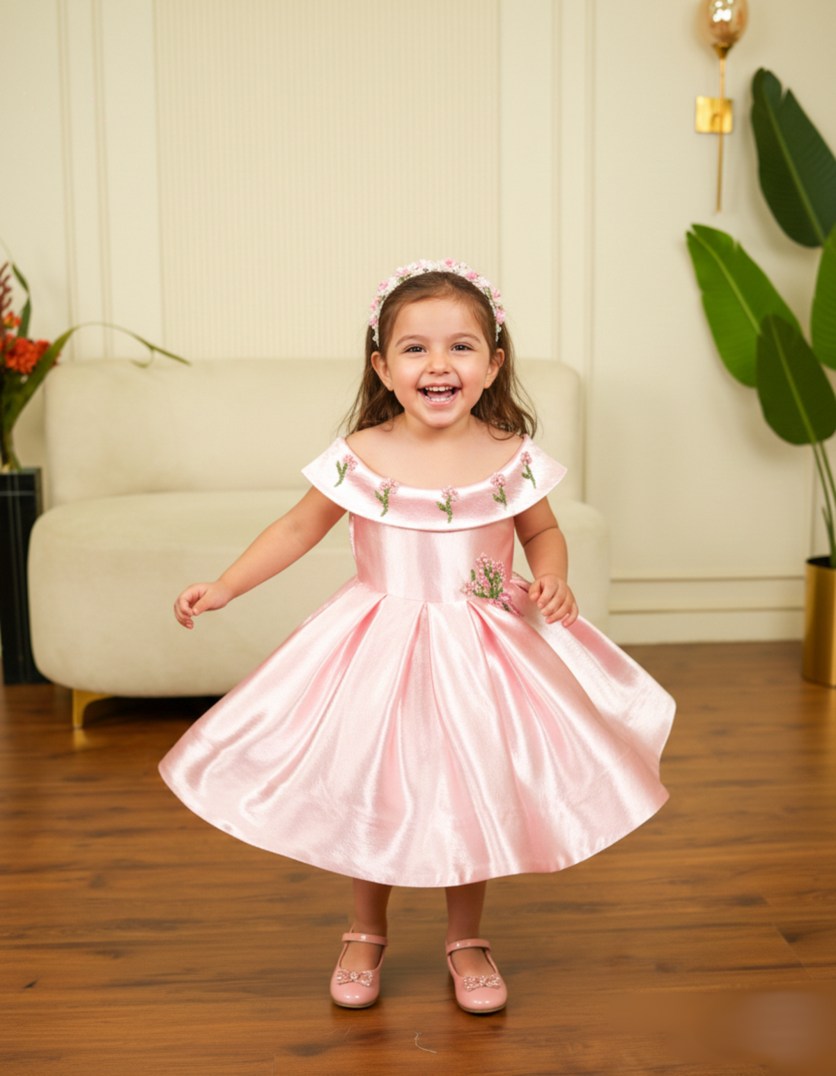 Young girl in a pink dress standing in a room with a couch and plants.