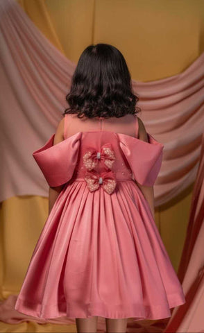 Pink dress with floral details on the back worn by a person, against a draped curtain background.